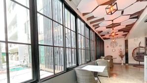 A modern interior with large windows, wicker furniture, and a unique ceiling design. - Le Cartier Guesthouse (Patong)
