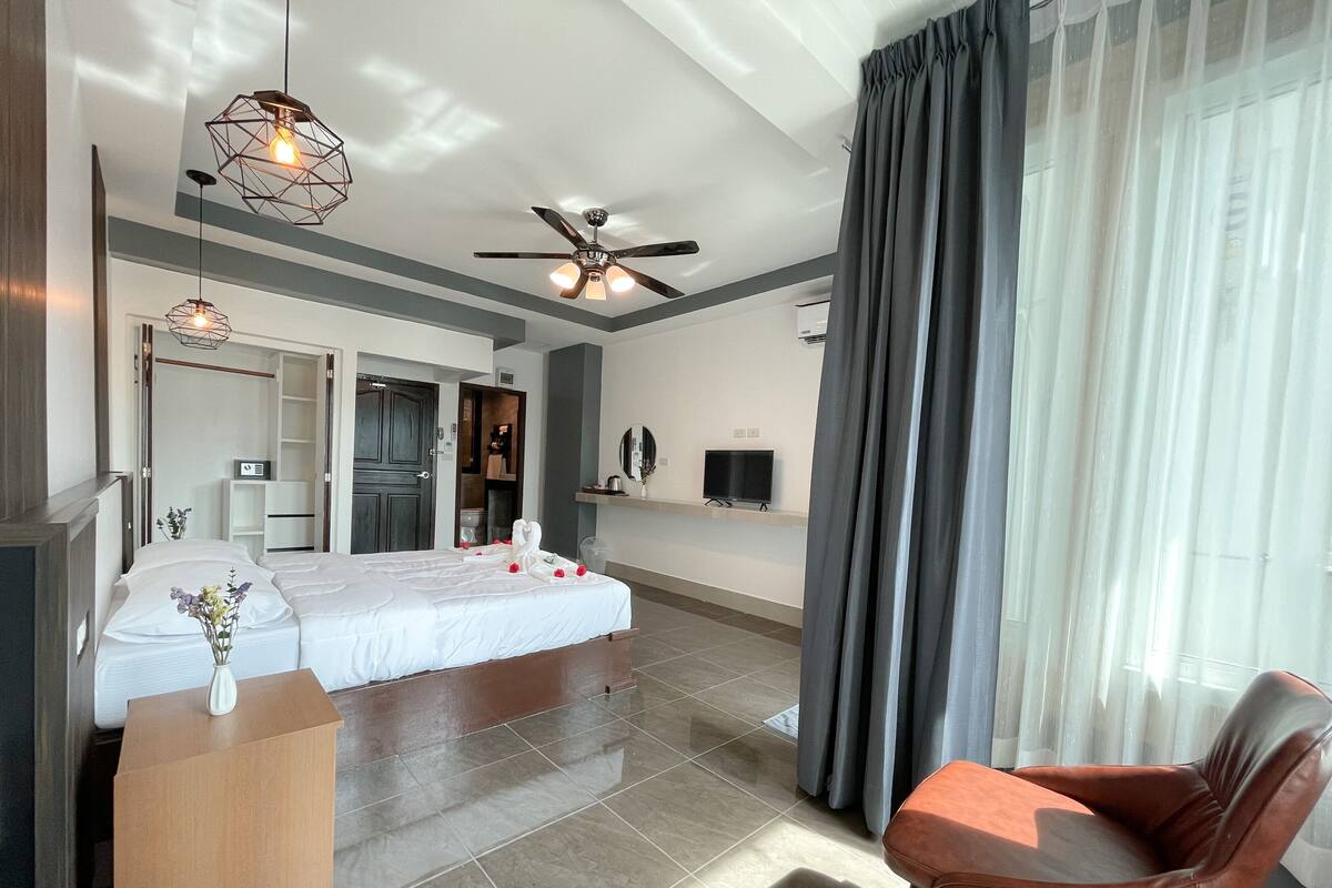 A modern hotel room with a large bed, a TV, a ceiling fan, and a seating area with a chair.