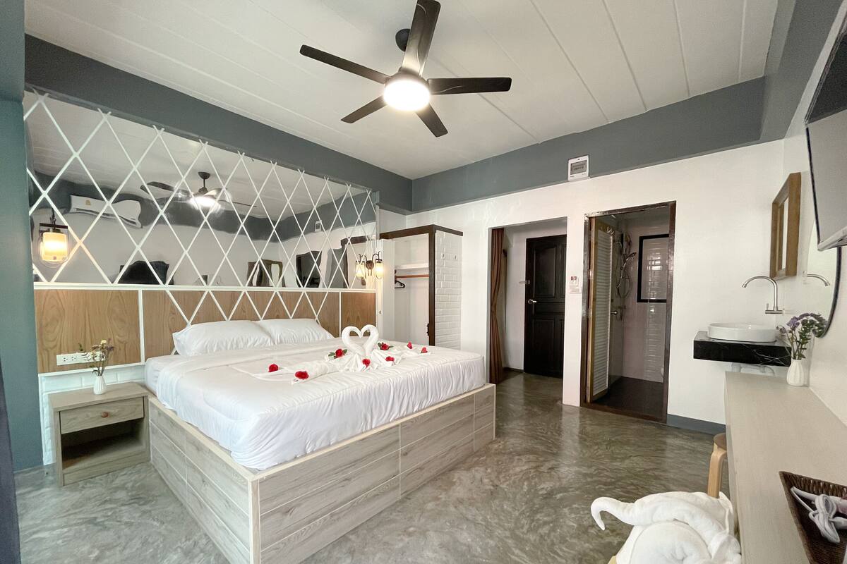 A modern hotel room with a large bed, a ceiling fan, a shower area, and a bathroom with a sink and mirror.