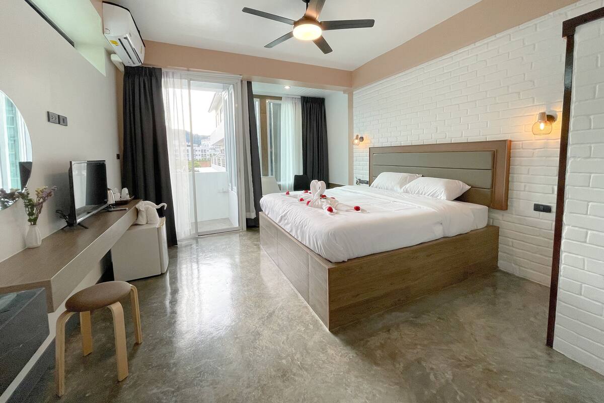 A hotel room with a bed, a desk, a chair, a TV, and a ceiling fan.
