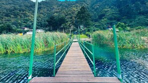 Eine Holzbrücke über Wasser mit Geländern, umgeben von Grünflächen und Hügeln.