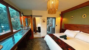 Ein Schlafzimmer mit einem großen Bett, einer Holzbank, einem Glastisch und Blick ins Freie.