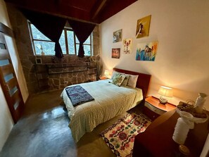 A cozy bedroom with a stone fireplace, a bed with a patterned bedspread, and artwork on the walls. - Guatemala Dreams Grand Chalet (San Lucas Tolimán)