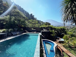 A swimming pool with lounge chairs, surrounded by lush greenery and a mountain in the background. - Guatemala Dreams Grand Chalet (San Lucas Tolimán)