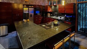 A modern kitchen with a large island, stone walls, wooden ceiling beams, and pendant lighting. - Guatemala Dreams Grand Chalet (San Lucas Tolimán)