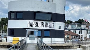 Ein Gebäude mit der Aufschrift "Harbour Master" und einer Treppe, die zu einer Tür führt, umgeben von einer Uferpromenade und Wohnhäusern.