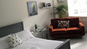 Ein Schlafzimmer mit einem Bett, einem roten Sofa, einem kleinen Tisch mit einer Pflanze und einem an der Wand befestigten Regal mit Büchern und einer Uhr.