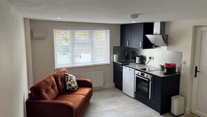 Eine kompakte Küche mit modernen Geräten, einer Couch und einem Fenster mit Jalousien.