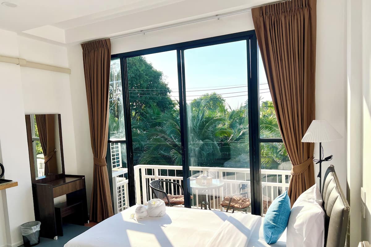 A hotel room with a large bed, a desk, a chair, a small table, and a balcony with a railing.