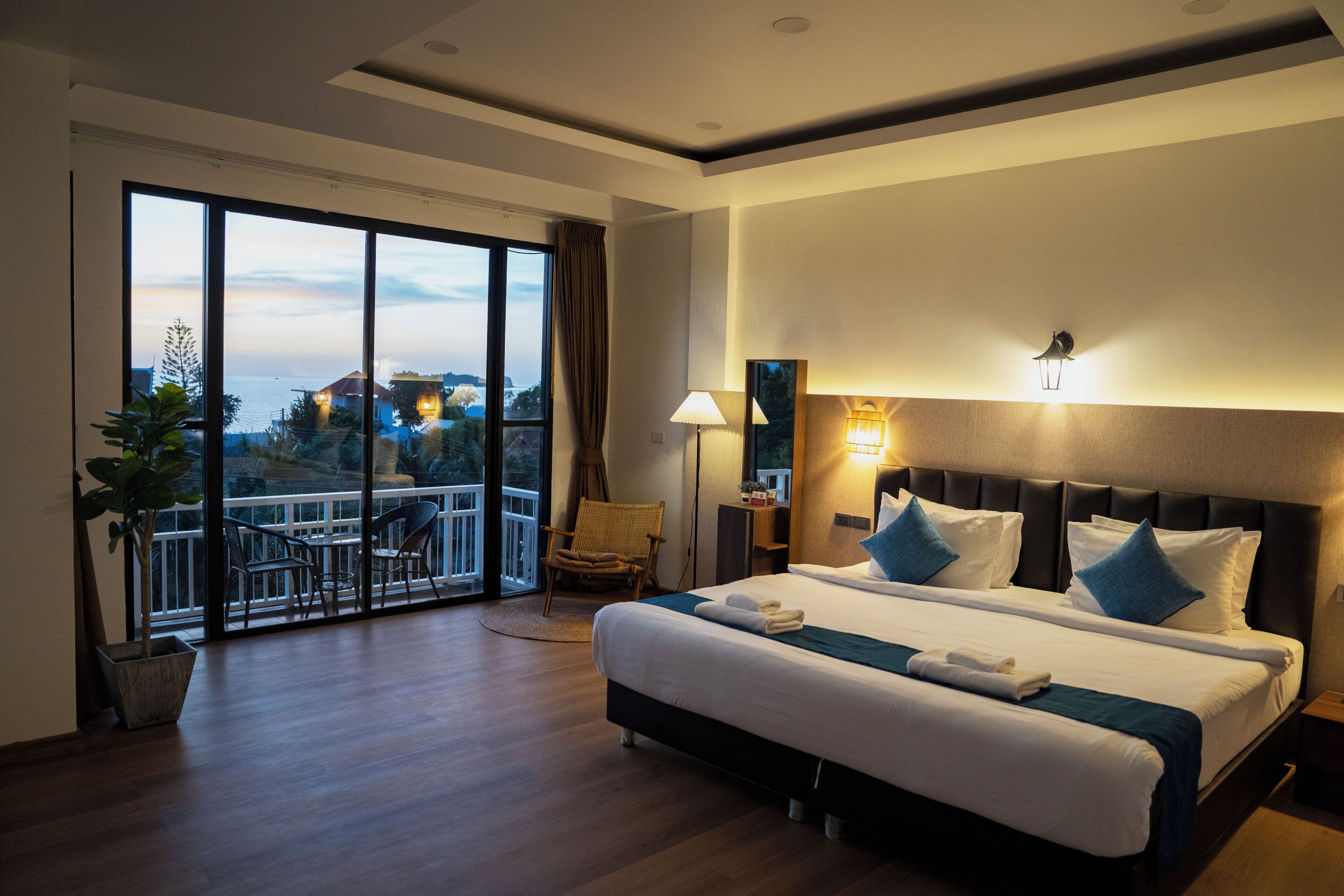 A hotel room with a large bed, a balcony with a view, and a nightstand with a lamp.