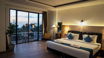 Una habitación de hotel con una cama grande, un balcón con vistas y una mesita de noche con lámpara.