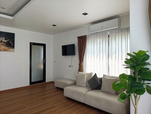 A modern living room with a sofa, a flat-screen TV, an air conditioning unit, and a wooden floor. - Serenity Bay Koh Samui (Koh Samui)