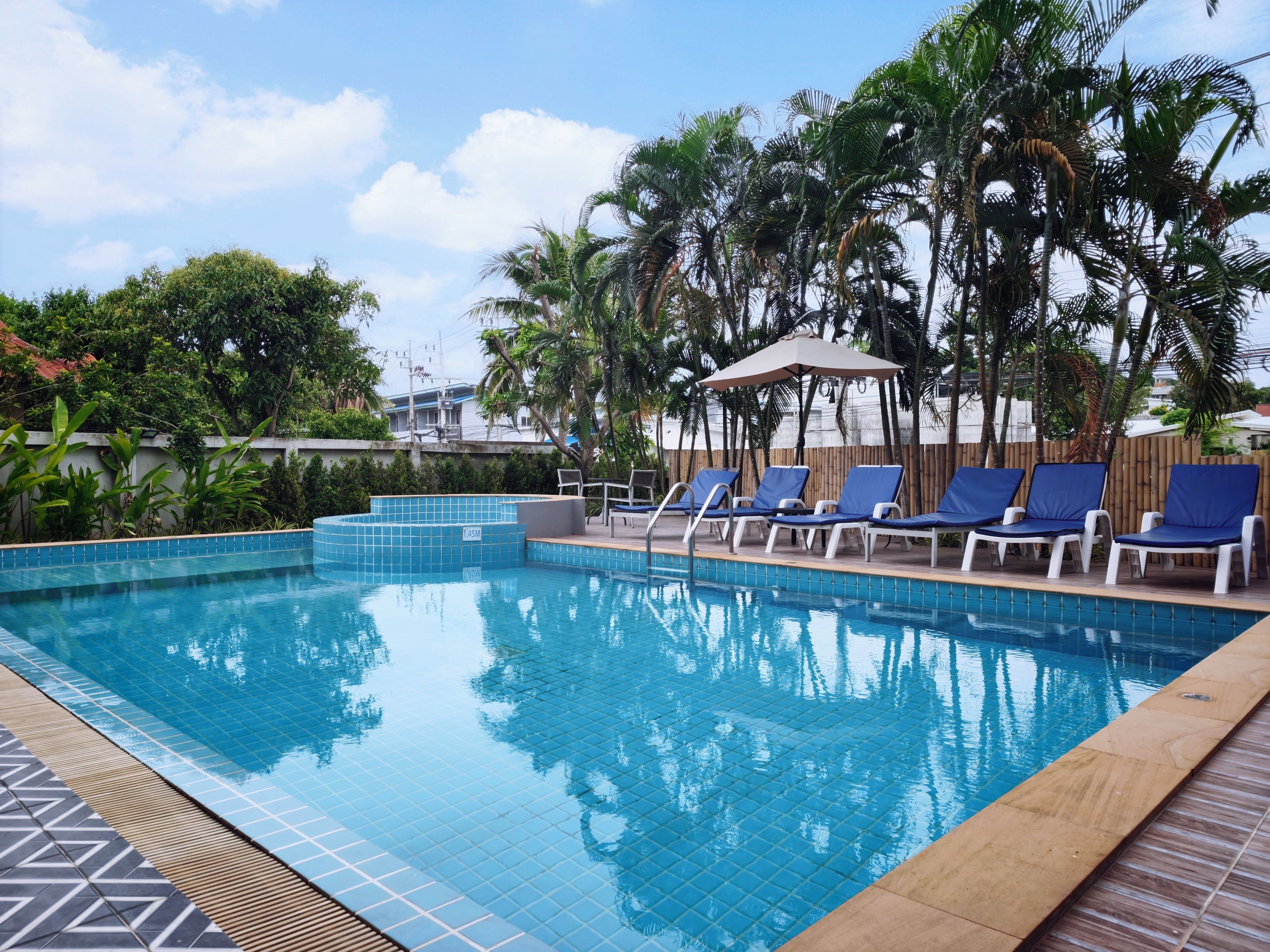 Una piscina con bordes de azulejos, rodeada de sillones de descanso y palmeras.