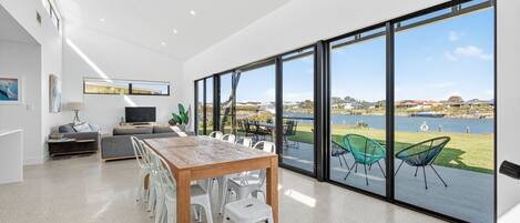 Ein moderner Essbereich mit großem Tisch und Stühlen, einer Couch, einem Fernseher und Seeblick durch große Fenster.