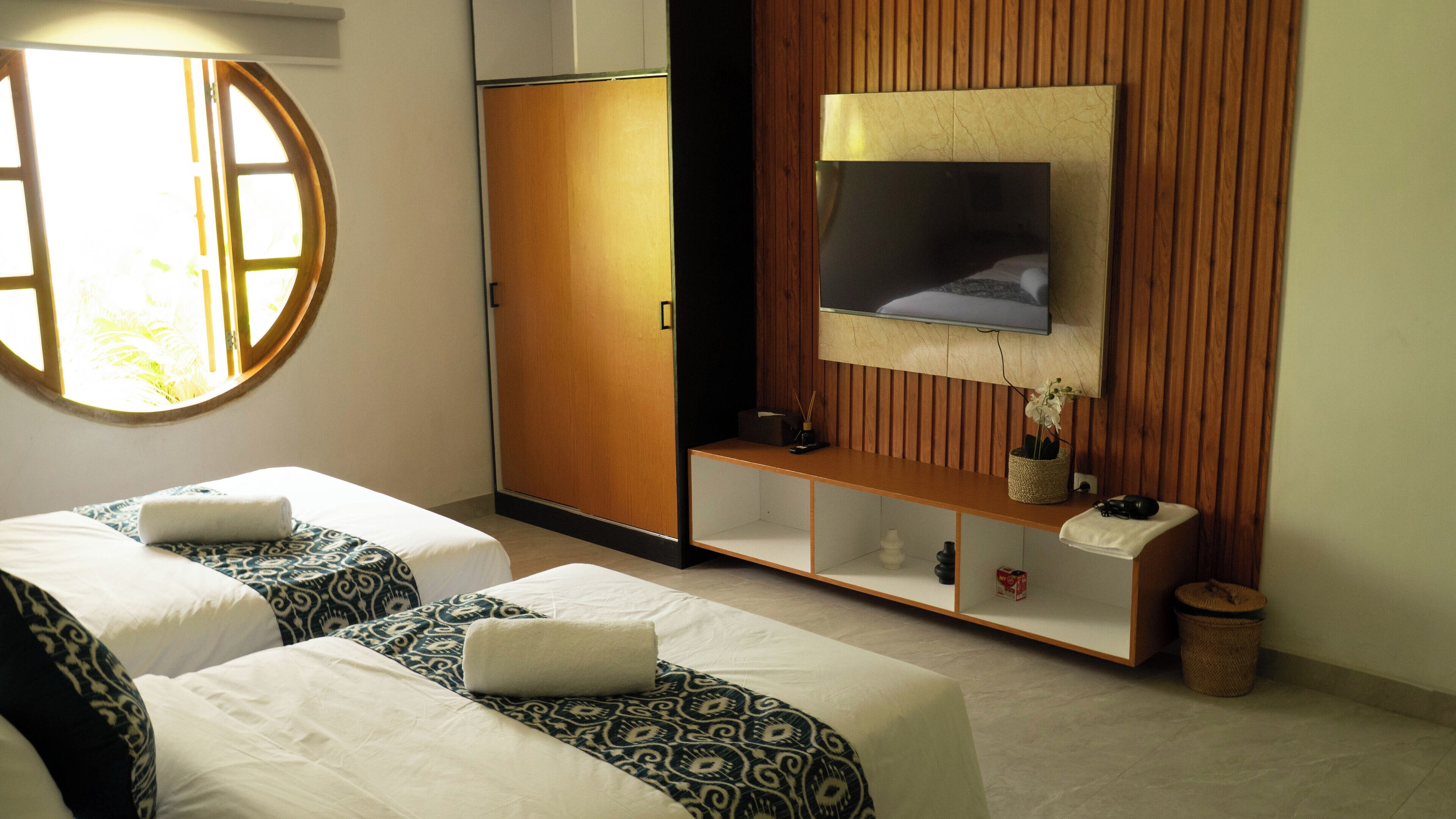 Une chambre d’hôtel avec deux lits, une armoire, une télévision et une petite étagère ornée d’objets décoratifs.