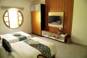 Habitación de hotel con dos camas, un armario, un televisor y un pequeño estante con objetos decorativos.