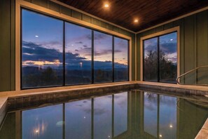 A swimming pool with large windows offering a view of a sunset over a mountainous landscape. - Sierra Splash Lodge | Pool/Theater | Sleeps 72 (Sevierville)