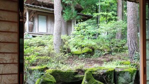 Una habitación japonesa tradicional con suelo de tatami, un celosía shoji y vistas a una zona boscosa con rocas y árboles.