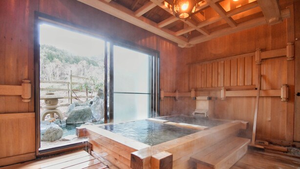 Un cuarto de spa de madera con aguas termales, piso de madera y vista a un área boscosa.