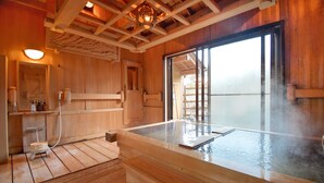 Un interior de madera con un baño de aguas termales, suelo de madera y un gran ventanal.