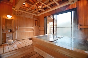A wooden interior with a hot spring bath, wooden flooring, and a large window.