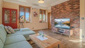 A living room with a sofa, a coffee table, a TV, and a brick wall.