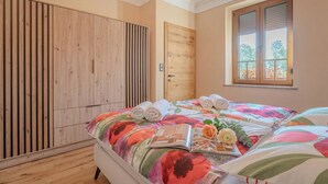 A bedroom with a bed, a wooden wardrobe, a window with a view, and a door.