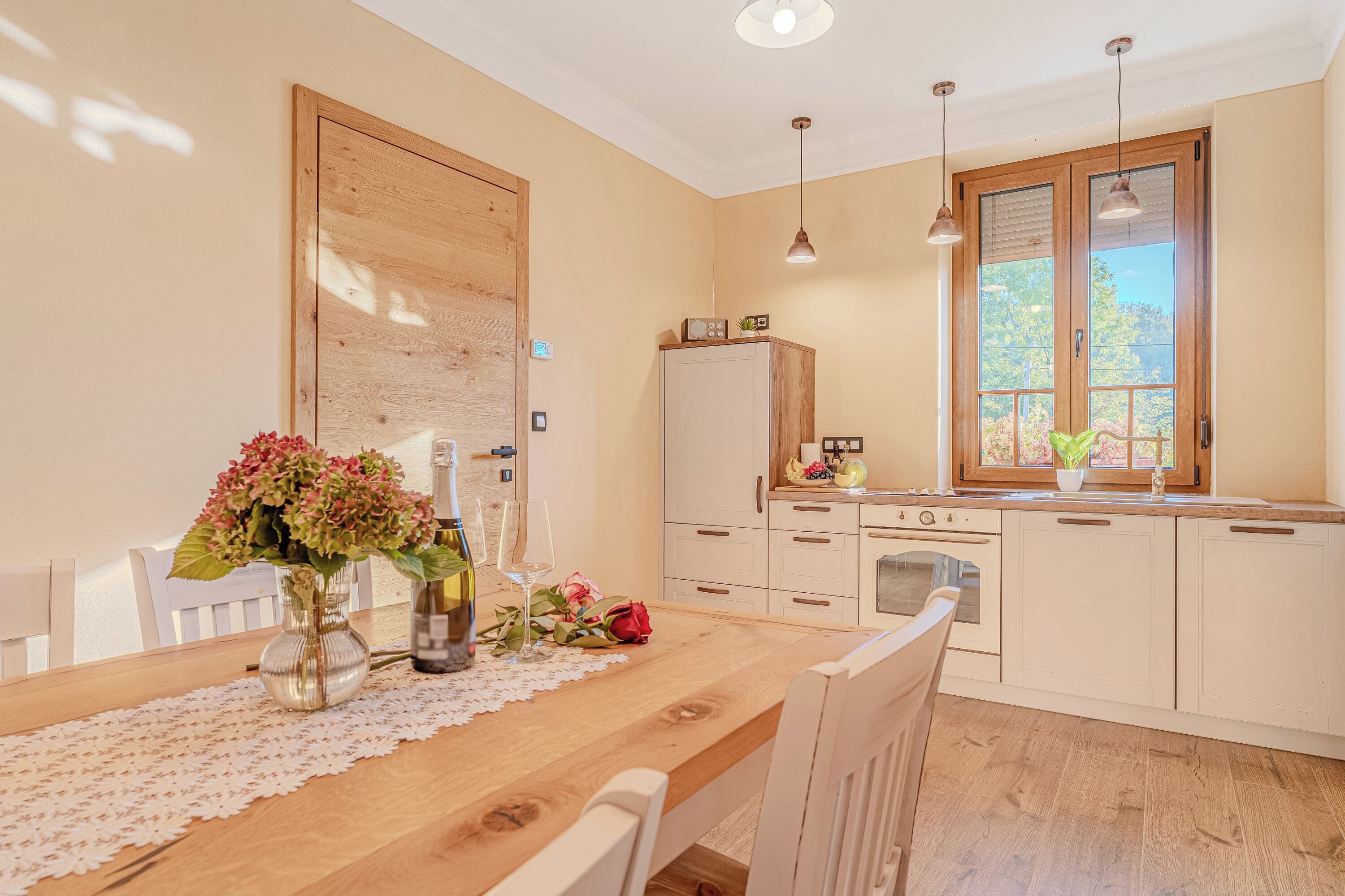 Une cuisine avec une table en bois, des placards blancs et une fenêtre donnant sur un paysage verdoyant.