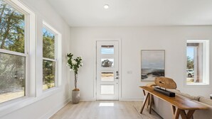 Una habitación amplia con ventanas grandes, un banco de madera, una puerta con paneles de vidrio y una obra enmarcadas en la pared.