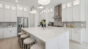 Una cocina moderna con armarios blancos, una isla grande de mármol y electrodomésticos de acero inoxidable.