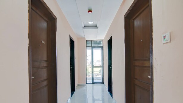 Un couloir avec deux portes en bois de chaque côté, une porte en verre au fond et un luminaire au plafond.