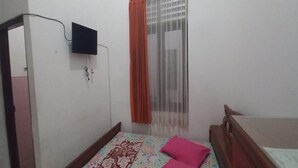 Une chambre à coucher avec un lit, un téléviseur fixé au mur et une fenêtre avec un rideau.