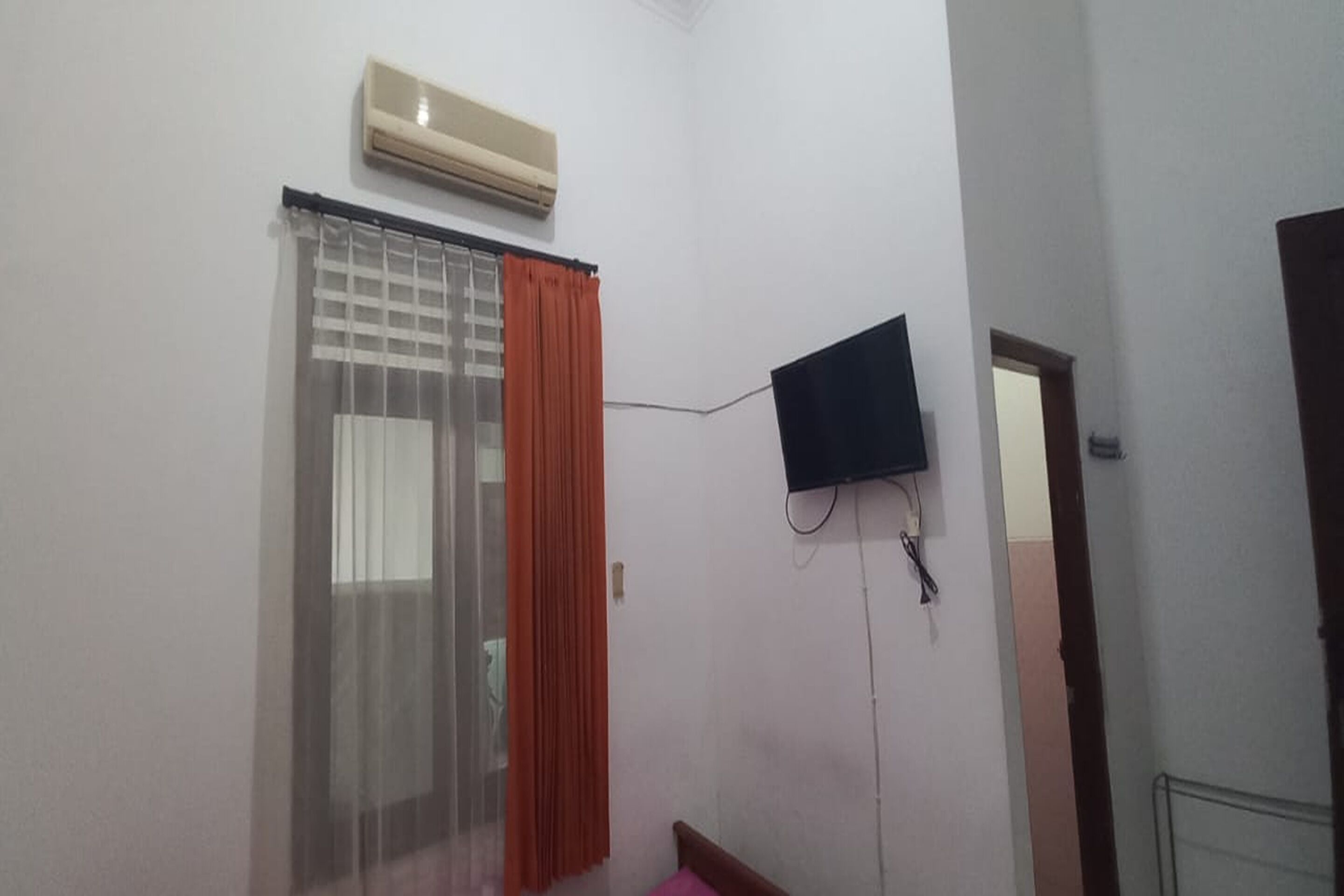 A room with a bed, a window with curtains, an air conditioning unit, and a mounted television.