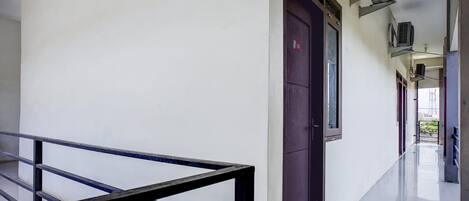 A corridor with a metal railing, a door with a red sign, and air conditioning units on the wall.