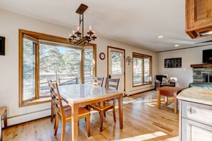 A spacious kitchen with large windows, a dining table, and wooden cabinetry. - Pineview House- Great  Location With a Hot Tub! (Estes Park)