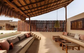 Un espace de détente extérieur doté d’un toit de chaume, d’une piscine et d’un aménagement comprenant un canapé et des tables.