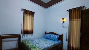 A small, well-lit bedroom with a single bed, a nightstand, and a wall-mounted lamp. - OYO 95055 Homestay Panasan Pak Budi (Sambi)