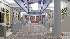 A hallway with a patterned floor, a red door at the end, and a blue wall with a green emblem. - OYO 95055 Homestay Panasan Pak Budi (Sambi)