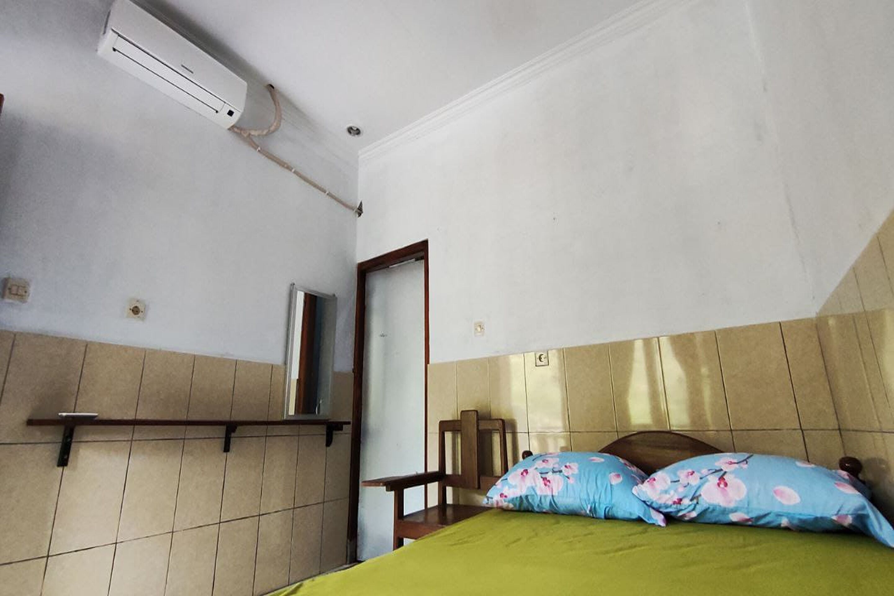 A room with a bed, a chair, a shelf, and an air conditioning unit.
