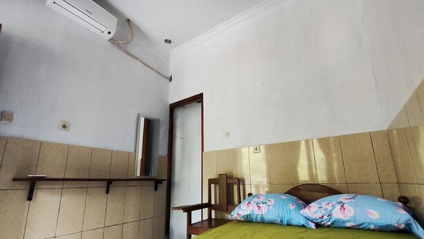 A room with a bed, a chair, a shelf, and an air conditioning unit. - OYO 95055 Homestay Panasan Pak Budi (Sambi)