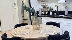 Moderni keittiö, jossa on valkoiset kaapit, ruostumattomasta teräksestä valmistettu jääkaappi ja musta työtaso.