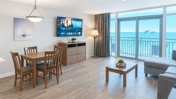 Une chambre d’hôtel moderne dotée d’un coin repas, d’un canapé, d’une télévision et d’un balcon offrant une vue sur la mer.