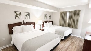 Une chambre d’hôtel avec deux lits, un plancher en bois, une table de chevet avec une lampe et une fenêtre avec des rideaux.