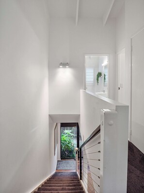 A staircase leading to a second floor with a white wall, a small window, and a plant. - Noosa River 2BD Townhouse - Modern & Stylish (Noosa)