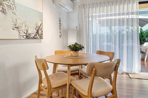 En matplats med ett runt träbord, fyra stolar, en krukväxt och en tavla på väggen.