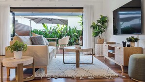 Una sala de estar moderna con sofá, mesa de centro y televisor, conectada a un balcón con plantas y una sombrilla.