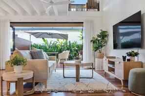A modern living room with a sofa, coffee table, and TV, connected to a balcony with plants and an umbrella. - Noosa River 2BD Townhouse - Modern & Stylish (Noosa)