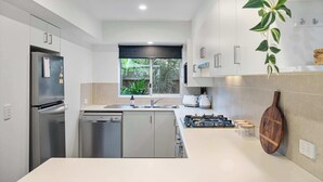 Una cocina moderna con electrodomésticos de acero inoxidable, lavavajillas, cocina a gas y ventana con vistas a zonas verdes.
