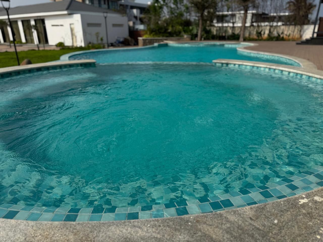 A swimming pool with a tiled edge, surrounded by a paved area and a building in the background.