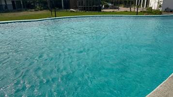 Una piscina con agua azul cristalina, rodeada por una cerca y edificios modernos al fondo.